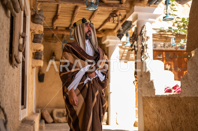 ارتداء الأزياء الشعبية في ذكرى تأسيس الدولة السعودية الاولى 22 فبراير، يوم بدينا 1727 م، الفخر والاعتزاز بالهوية السعودية، المناسبات والأعياد الوطنية، رجل عربي خليجي سعودي يرتدي العقال والبشت التقليدي في منزل طيني قديم