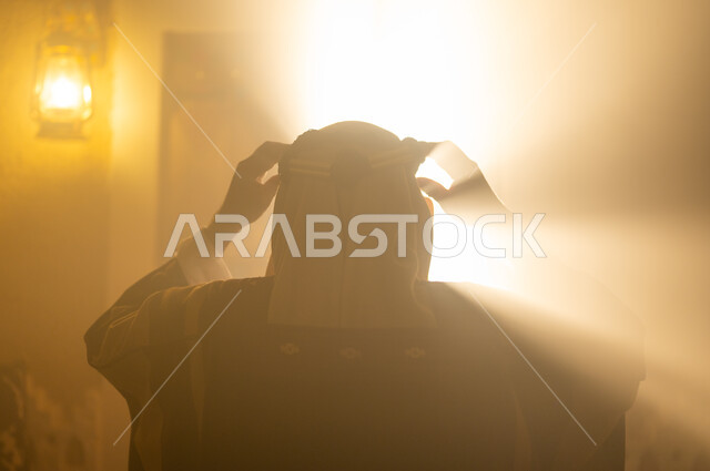 Elegance and attention to external appearance, the concept of nobility, pride, and pride, national holidays and events, the anniversary of the founding of the first Saudi state, February 22, a close-up picture from the back of a Saudi Gulf Arab man wearing a bisht and headband, adjusting his clothes, standing next to the window, Day of Dina 1727 A