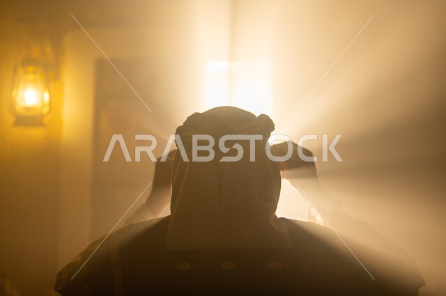 Elegance and attention to external appearance, the concept of nobility, pride, and pride, national holidays and events, the anniversary of the founding of the first Saudi state, February 22, a close-up picture from the back of a Saudi Gulf Arab man wearing a bisht and headband, adjusting his clothes, standing next to the window, Day of Dina 1727 A