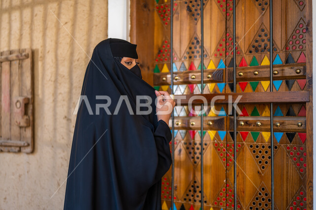 ذكرى تأسيس الدولة السعودية الاولى 22 فبراير، إظهار الجمال العربي البدوي للنساء السعوديات، نمط حياة البدو الشعبية في البيوت الطينية التراثية، يوم بدينا 1727 م، ارتداء الزي الشعبي، صورة من الجانب لامرأة عربية خليجية سعودية ترتدي العباءة السوداء والبرقع في منزل قديم