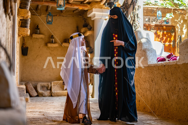 تبادل الأحاديث والدردشات، ذكرى تأسيس الدولة السعودية 1727 م، تربيه الأبناء على حب الوطن، امرأة عربيه خليجيه سعوديه ترتدي البرقع والعباءه السوداء تمسك بيد ابنها وتمشي في إحدى البيوت التراثيه القديمة، ارتداء الأزياء الشعبيه التقليدية في المناسبات والأعياد الوطنية