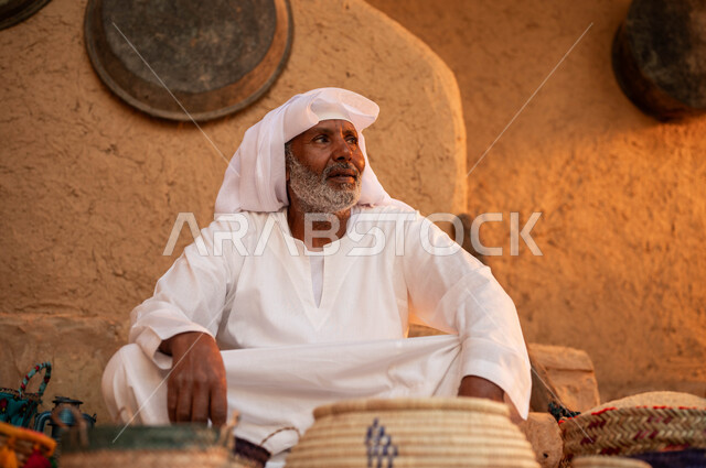 الاعتزاز والفخر بالتراث السعودي، عرض الحبوب والبقوليات سلل من الحصير اليدوي، يوم بدينا 22 فبراير، بائع عربي خليجي سعودي يرتدي الزي التقليدي يجلس على بساط شعبي، بيع المنتجات المحليه الوطنيه، ذكرى تأسيس الدولة السعودية الأولى 1727 م