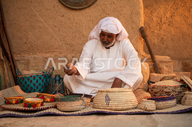 عرض الحبوب والبقوليات سلل من الحصير اليدوي، يوم بدينا 22 فبراير، الاعتزاز والفخر بالتراث السعودي، بائع عربي خليجي سعودي يرتدي الزي التقليدي يجلس على بساط شعبي، بيع المنتجات المحليه الوطنيه، ذكرى تأسيس الدولة السعودية الأولى 1727 م
