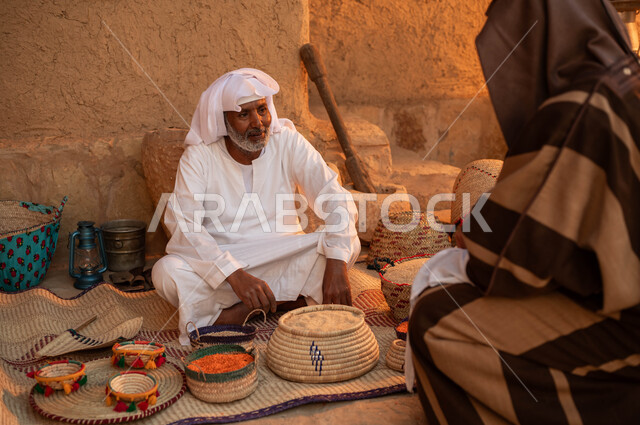 عرض المنتجات و الحبوب المحليه الوطنيه في سلل من الحصير اليدوي, يوم بدينا 1727م, ذكرى تأسيس الدولة السعودية الأولى في 22 فبراير، صورة من الخلف لرجل يقوم بالشراء من بائع عربي خليجي سعودي يرتدي الزي التقليدي يقوم ببيع العدس و البقوليات على بساط شعبي