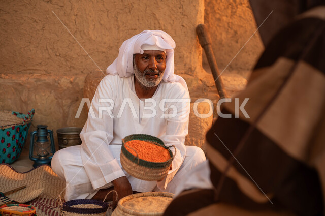 ذكرى تأسيس الدولة السعودية الأولى في 22 فبراير، صورة من الخلف لرجل يقوم بالشراء من بائع عربي خليجي سعودي يرتدي الزي التقليدي يقوم ببيع العدس و البقوليات على بساط شعبي ،عرض المنتجات و الحبوب المحليه الوطنيه في سلل من الحصير اليدوي، يوم بدينا 1727م