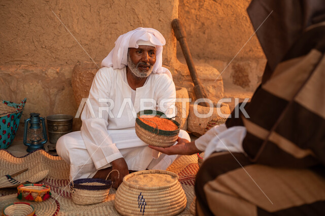 يوم بدينا 1727م, ذكرى تأسيس الدولة السعودية الأولى في 22 فبراير، صورة من الخلف لرجل يقوم بالشراء من بائع عربي خليجي سعودي يرتدي الزي التقليدي يقوم ببيع العدس و البقوليات على بساط شعبي ،عرض المنتجات و الحبوب المحليه الوطنيه في سلل من الحصير اليدوي