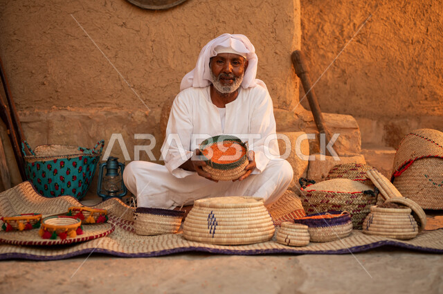 الاعتزاز و الفخر بالتراث السعودي، بيع الحبوب و البقوليات على بساط شعبي، يوم بدينا 22 فبراير، بائع عربي خليجي سعودي يرتدي الزي التقليدي و يحمل بيده سلة من الحصير اليدوي مليئة بالعدس ،عرض المنتجات المحليه الوطنيه ،ذكرى تأسيس الدولة السعودية الأولى 1727 م