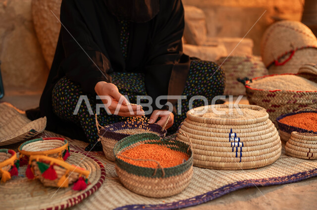المحافظة على التراث السعودي ،صورة مقربة لبائعه عربيه خليجية سعودية ترتدي العباءه السوداء تقوم  ببيع العدس و البقوليات على بساط شعبي ،عرض الحبوب والمنتجات المحليه الوطنيه في سلل من الحصير اليدوي ، يوم بدينا 22 فبراير، ذكرى تأسيس الدولة السعودية الأولى 1727 م