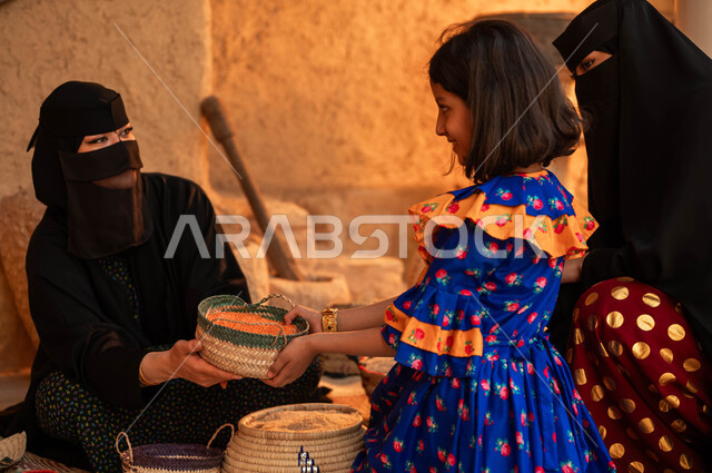 عرض الحبوب والمنتجات المحليه الوطنيه في سلل من الحصير اليدوي ،إمرأه مع ابنتها تقوم بالشراء من بائعه عربية خليجية سعودية ترتدي البرقع والعباءة السوداء تقوم ببيع العدس و البقوليات على بساط شعبي، يوم بدينا 1727 م، ذكرى يوم تأسيس الدولة السعودية الأولى 22 فباير