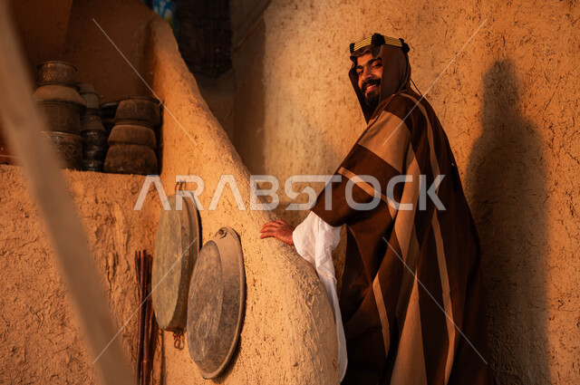 يوم بدينا 1727 م ،الوقوف على درج مبني من الطين في احد البيوت التراثية، ذكرى تأسيس الدولة السعودية الاولى 22 فبراير ،ارتداء الأزياء الشعبيه في الأعياد الوطنية ،صورة من الخلف لرجل عربي خليجي سعودي يرتدي الزي التقليدي ينظر الى الكاميرا بايماءات السرور