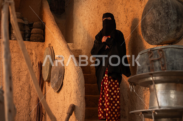 الاعتزاز والفخر بالهوية السعودية ،ارتداء الأزياء الشعبيه للمناسبات والأعياد الوطنية ،ذكرى تأسيس الدولة السعودية الاولى 1727 م، يوم بدينا 22 فبراير، امرأة عربية خليجية سعودية ترتدي البرقع والعباءة السوداء تقف على درج مبني من الطين في احد البيوت التراثيه القديمة