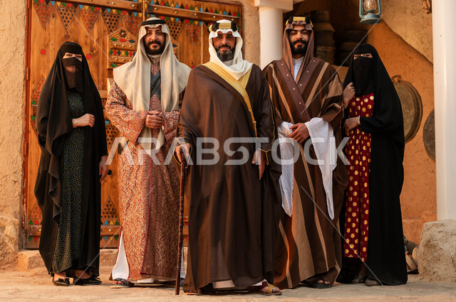 النظر إلى الكاميرا بإيماءات الاعتزاز بالهوية الوطنيه، يوم بدينا 1727 م، دور النساء والرجال في توحيد المملكه، عائلة عربيه خليجية سعودية ترتدي الأزياء الشعبية في الأعياد الوطنية يقفون في أحد البيوت التراثية االطينية، ذكرى تأسيس الدولة السعودية الأولى 22 فبراير