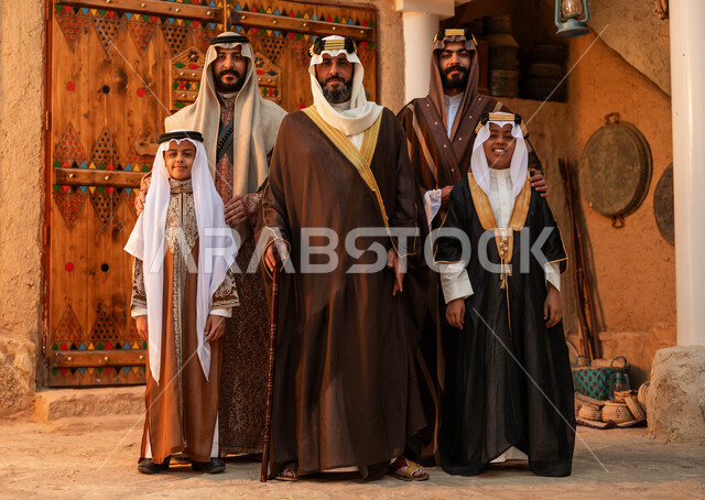 النظر إلى الكاميرا بتعابير السرور، المحبة بين افراد الأسرة ،ذكرى تأسيس الدولة السعودية الأولى 22 فبراير ،مجموعه من الرجال العرب الخليجيون السعوديون مع أبنائهم يرتدون الأزياء الشعبية في الأعياد الوطنية ،الوقوف في أحد البيوت التراثية الطينية ،يوم بدينا 1727 م