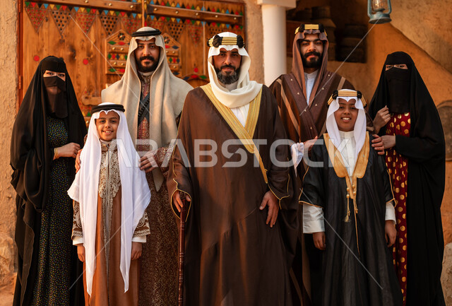 النظر إلى الكاميرا بإيماءات الفخر بالهوية الوطنيه، المحبة بين افراد الأسرة ،ذكرى تأسيس الدولة السعودية الأولى 22 فبراير ،العائلات العربيه الخليجية السعودية ترتدي الأزياء الشعبية في الأعياد والمناسبات الوطنية ،الوقوف في أحد البيوت التراثية الطينية ،يوم بدينا 1727 م