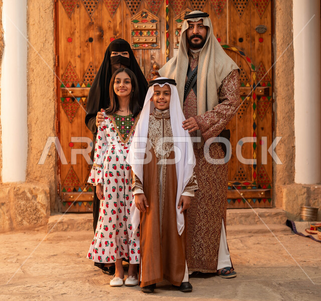 يوم بدينا 1727 م، النظر إلى الكاميرا بإيماءات الاعتزاز و الفخر بالهوية السعودية، ذكرى تأسيس الدولة السعودية الأولى 22 فبراير، عائلة عربيه خليجية سعودية ترتدي الأزياء الشعبية في الأعياد والمناسبات الوطنية يقفون في أحد البيوت التراثية المبنية من الطين