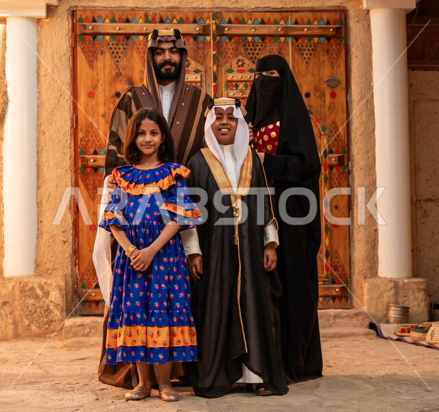 النظر إلى الكاميرا بإيماءات الاعتزاز و الفخر بالهوية السعودية، ذكرى تأسيس الدولة السعودية الأولى 1727 م، عائلة عربيه خليجية سعودية ترتدي الأزياء الشعبية في الأعياد والمناسبات الوطنية يقفون في أحد البيوت التراثية المبنية من الطين، مفهوم حب الوطن والانتماء اليه