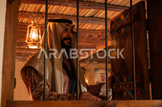 Wearing popular costume on the anniversary of the founding of the first Saudi state, February 22, heritage houses built in the old style, national holidays and events, Day of Our Day 1727 AD, pride and pride in Saudi identity, a close-up photo of a Saudi Gulf Arab man wearing a dakhla and aqal and looking at something