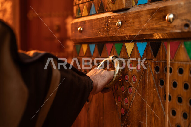 الأصالة و الحضارة والعراقة، يوم بدينا 1727 م، ذكرى تأسيس الدولة السعودية الاولى 22 فبراير، الاحتفال في الأعياد والمناسبات الوطنية، صورة مقربة ليد رجل كبير السن عربي خليجي سعودي يرتدي أزياء التأسيس يقوم بطرق الباب، الأبواب الخشبية المزخرفة