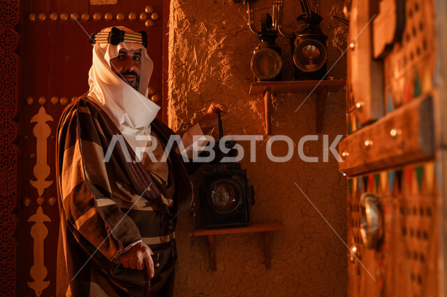 مفهوم الحضارة والأصالة والعراقة، توارث حب التراث القديم من الأجداد، ذكرى تأسيس الدولة السعودية الاولى 22 فبراير، يوم بدينا 1727 م، صورة مقربة لرجل عربي خليجي سعودي يرتدي أزياء التأسيس ينظر إلى الكاميرا يمسك بيده فانوس معدني، المناسبات والأعياد الوطنية