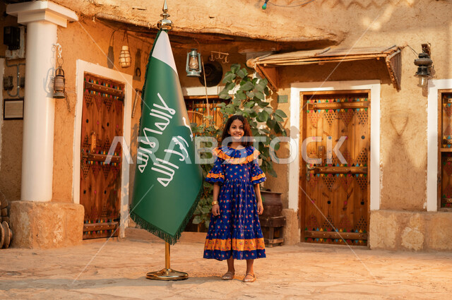 المحافظة على التراث السعودي، الوقوف بإيماءات الفخر والاعتزاز، يوم بدينا 1727 م، ذكرى تأسيس الدولة السعودية الاولى 22 فبراير، فتاة عربيه خليجية سعودية مبتسمة ترتدي الأزياء الشعبية تقف بجانب علم التأسيس، المناسبات والأعياد الوطنية، تربيه الأبناء على حب الوطن