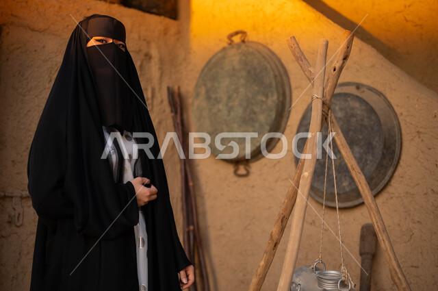 استخدام خضاضة اللبن لصنع السمن والزبدة قديما، ذكرى تأسيس الدولة السعودية الاولى 22 فبراير، مهن وأعمال يدوية نسائية، يوم بدينا 1727م، نمط الحياة في البيوت الطينية التراثية الشعبية، امرأة عربية خليجية سعودية ترتدي البرقع والعباءة السوداء تنظر إلى الكاميرا