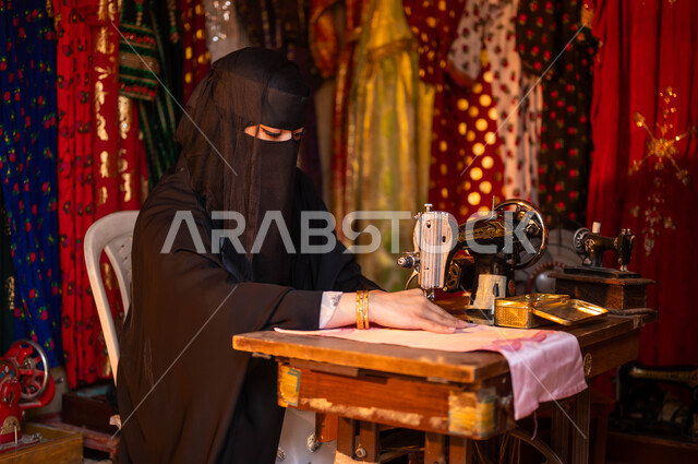 حرف وأعمال ومهن تقليدية نسائية, خياطة عربية سعودية خليجية ترتدي العباءة السوداء والبرقع تقوم بحياكة وخياطة القماش على الماكينة اليدوية، ذكرى تأسيس الدوله السعوديه الاولى 22 فبراير، يوم بدينا 1727 م، الأسواق الشعبيه في الأحياء القديمة