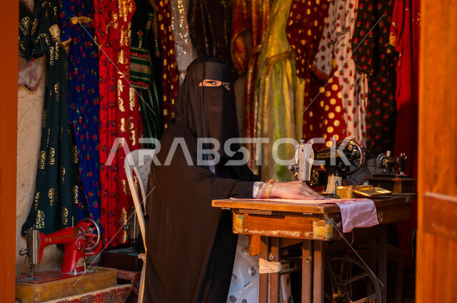 حياكة وخياطة القماش على الماكينة اليدوية، تصميم الأزياء الشعبية التراثية، حرف وأعمال ومهن تقليدية نسائية, خياطة عربية سعودية خليجية ترتدي العباءة السوداء والبرقع تنظر إلى الكاميرا، ذكرى تأسيس الدوله السعوديه الاولى 22 فبراير، يوم بدينا 1727 م