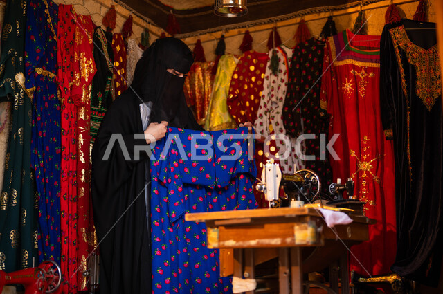تصميم وتجهيز الأزياء الشعبية التراثية للمناسبات الوطنية، حرف ومهن تقليدية نسائية, امرأة عربية سعودية خليجية ترتدي العباءة السوداء والبرقع،  حياكة وخياطة القماش على الماكينة اليدوية، ذكرى تأسيس الدوله السعوديه الاولى 22 فبراير، يوم بدينا 1727 م