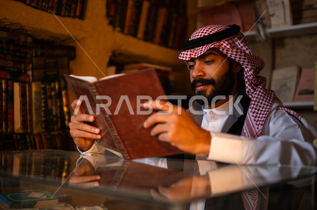 ممارسة هواية المطالعة, أماكن بيع الكتب والمستلزمات المكتبية, المكتبات القديمة في الأحياء التراثية الطينية، يوم بدينا 1727 م، ذكرى تأسيس الدولة السعودية الأولى 22 فبراير، صورة مقربة لشاب عربي خليجي سعودي يرتدي الزي التقليدي يقوم بقراءة كتاب بإيماءات التركيز