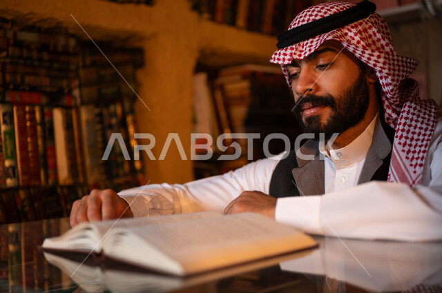 Anniversary of the founding of the first Saudi state, February 22, love and passion for culture and knowledge, places that sell books and office supplies, old libraries in the mud heritage neighborhoods, Day of Dina 1727 AD, a close-up photo of a young Saudi Gulf Arab man wearing traditional clothing reading a book with gestures of concentration