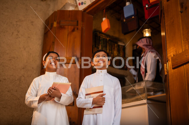 ممارسة هواية القراءة, مكتبة لبيع المستلزمات المكتبية, المكتبات القديمة في الأحياء التراثية الطينية، يوم بدينا 1727 م، ذكرى تأسيس الدولة السعودية الأولى 22 فبراير، ولدان عربيان خليجيان سعوديان يرتديان الثوب التقليدي والقبعة البيضاء ويحملان الكتب بإيماءات السرور
