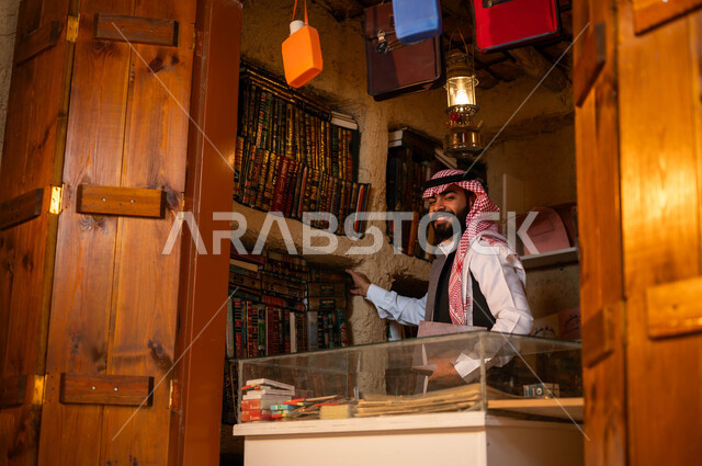 مكان الهواة ومحبي القراءة, المكتبات القديمة في الأحياء التراثية الطينية, دكان قديم لبيع الكتب والمستلزمات المكتبية، يوم بدينا 1727 م، ذكرى تأسيس الدولة السعودية الأولى 22 فبراير، شاب عربي خليجي سعودي مبتسم يرتدي الزي التقليدي ينظر إلى الكاميرا