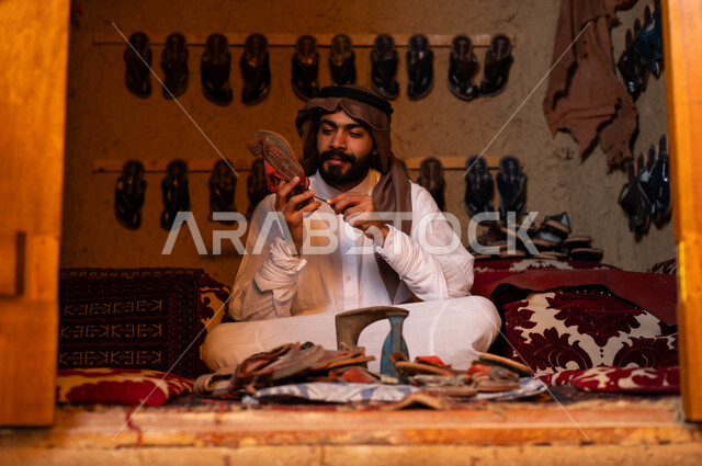 ذكرى تأسيس الدولة السعودية الأولى في 22 فبراير, يوم بدينا 1727م, ممارسة المهن الشعبية التقليدية وإحياء التراث الخليجي, الصناعات والحرف المتوارثة من الأجداد, اسكافي عربي خليجي سعودي يرتدي الزي التقليدي يقوم بإصلاح الأحذية باستخدام الأدوات المناسبة