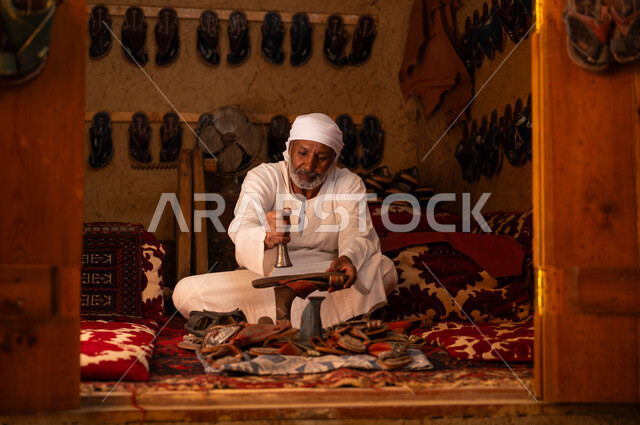 التمسك بالصناعات والحرف الخليجية, توارث المهن التقليدية من الأجداد, مفهوم إحياء التراث الشعبي, اسكافي مسن عربي خليجي سعودي يرتدي الزي التقليدي يقوم باستخدام الأدوات المناسبة لصناعة وتصليح الأحذية, يوم بدينا 1727م, ذكرى تأسيس الدولة السعودية الأولى في 22 فبراير