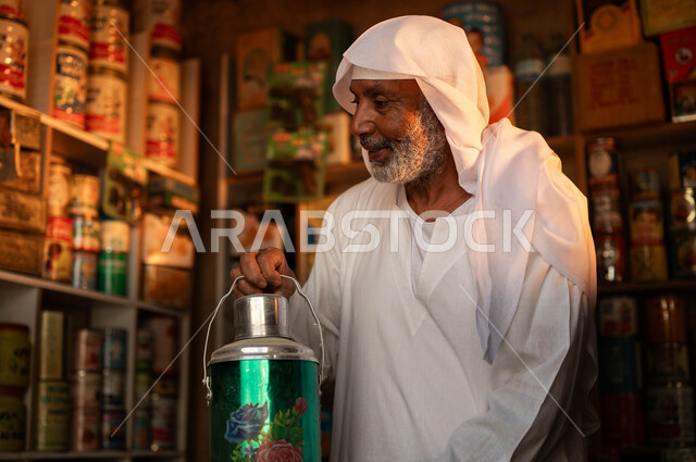 Old popular shops, a close-up of an elderly smiling Saudi Gulf Arab man wearing traditional clothing holding a container of hot drinks, places selling household supplies in Saudi heritage markets, Day of Our Day 1727 AD, the anniversary of the founding of the first Saudi state on February 22