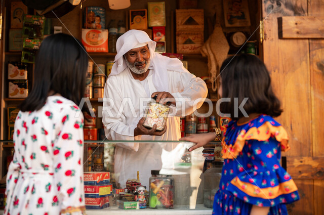 يوم بدينا 1727م, صورة من الخلف لبنتين عربيتين خليجيتين سعوديتين ترتديان الزي التقليدي تقومان بشراء الحلوى من الدكان, ذكرى تأسيس الدولة السعودية الأولى في 22 فبراير, محلات تجارية شعبية في الأسواق والأحياء السعودية القديمة