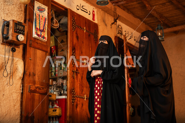 ذكرى تأسيس الدولة السعودية الأولى في 22 فبراير, الأحياء التراثية الشعبية, ارتداء الزي التقليدي الشعبي في الأعياد والمناسبات الوطنية, سيدتان عربيتان خليجيان سعوديتان ترتديان البرقع والعباءة السوداء تتجولان في إحدى الأسواق القديمة, يوم بدينا 1727م