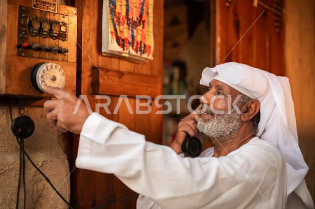 Anniversary of the founding of the first Saudi state on February 22, antiques and old devices, Our Day 1727 AD, traditional tools and means of communication in Saudi Arabia, rare Gulf folk and instruments, a close-up of an elderly smiling Saudi Gulf Arab man wearing traditional clothing using a landline phone