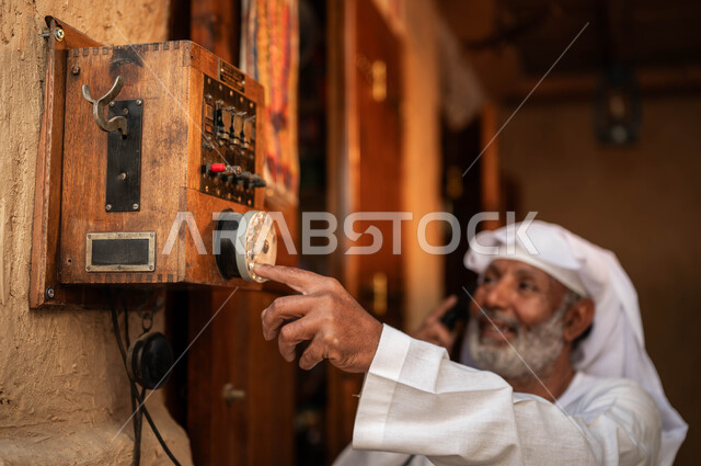 يوم بدينا 1727م, ذكرى تأسيس الدولة السعودية الأولى في 22 فبراير, أنتيكا وأجهزة قديمة, أدوات ووسائل الاتصال التقليدية في السعودية, شعبيات وآلات خليجية نادرة, صورة مقربة لرجل كبير بالسن عربي خليجي سعودي مبتسم يرتدي الزي التقليدي يقوم باستخدام الهاتف الأرضي