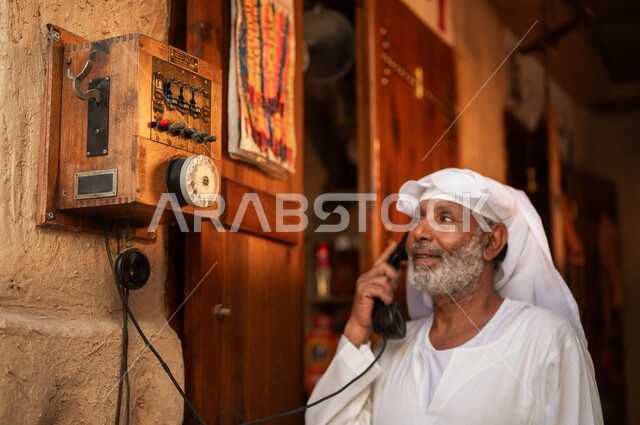 Antiques and old devices, traditional tools and means of communication in Saudi Arabia, rare Gulf folklore and instruments, a close-up photo of an old Saudi Gulf Arab man wearing traditional clothing talking on the landline, a day of our life 1727 AD, the anniversary of the founding of the first Saudi state on February 22
