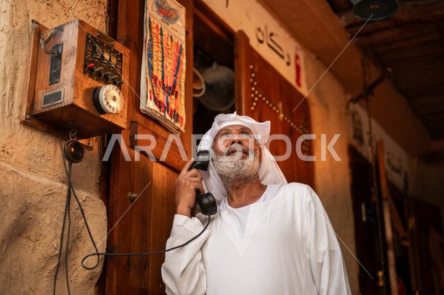 أدوات ووسائل الاتصال التقليدية في السعودية, شعبيات وآلات خليجية نادرة, صورة مقربة لرجل كبير بالسن عربي خليجي سعودي يرتدي الزي التقليدي يقوم بالتحدث عبر الهاتف الأرضي, يوم بدينا 1727م, ذكرى تأسيس الدولة السعودية الأولى في 22 فبراير، أنتيكا وأجهزة قديمة