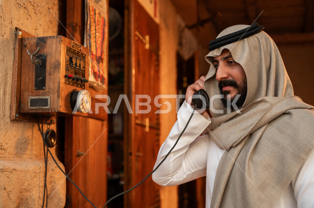 وسائل اتصال تقليدية في السعودية، شعبيات وأدوات خليجية نادرة, أنتيكا وأجهزة قديمة, ذكرى تأسيس الدولة السعودية الاولى 22 فبراير، صورة مقربة لشاب عربي خليجي سعودي يرتدي الزي التقليدي يقوم باستخدام الهاتف الأرضي في إحدى الأسواق الشعبية, يوم بدينا 1727م