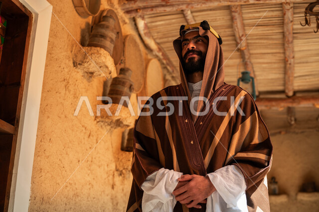 التمسك بالتراث السعودي, ارتداء الأزياء الشعبية التقليدية في الأعياد والمناسبات الوطنية, صورة مقربة لشاب عربي خليجي سعودي مبتسم يرتدي البشت والعقال يتجول في المناطق التراثية الطينية القديمة, يوم بدينا 1727م, ذكرى تأسيس الدولة السعودية الأولى في 22 فبراير