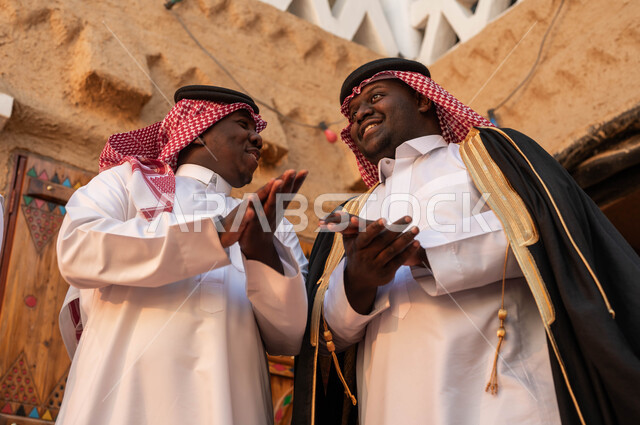 Gestures of happiness and joy, ancient clay heritage revivals, popular Najdi parade costumes, participation in national events, holidays and festivals, a picture from below of two Arab men, two Saudi Gulf Arabs, celebrating the anniversary of the founding of the Saudi state, February 22, the day of our religion 1727.