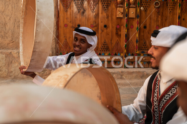 النظر إلى الكاميرا بإيماءات السعادة، إظهار الولاء والحب للدولة السعودية، الأحياء التراثية الطينية القديمة، صورة مقربة لرجل عربي خليجي سعودي يقوم بالاحتفال بتأسيس الدولة الأولى، الرقص الشعبي وقرع الطبول احتفالا بيوم بدينا ١٧٢٧، ارتداء ازياء العرضه النجدية