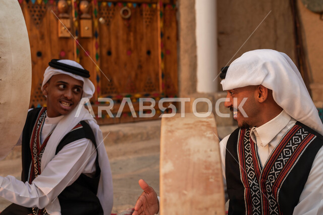 النظر بإيماءات السعادة والاندماج مع الرقص الشعبي وقرع الطبول احتفالا بيوم بدينا ١٧٢٧، إظهار الولاء والحب للدولة السعودية، صورة مقربة لرجل عربي خليجي سعودي يقوم بقرع الطبول احتفالا بتأسيس الدولة الأولى، الأحياء التراثية الطينية القديمة، ارتداء ازياء العرضه النجدية