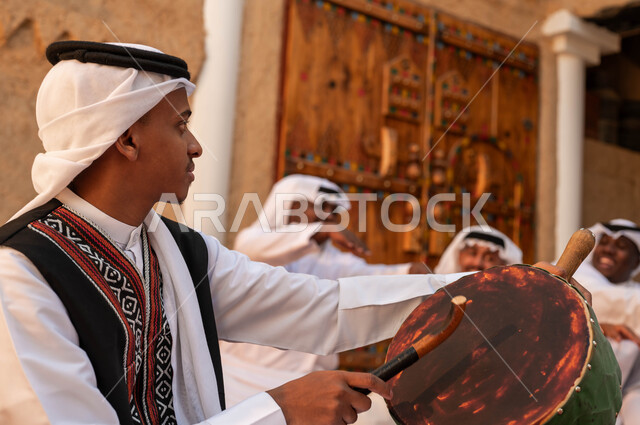 عروض الفلكلور التراثي، إظهار الولاء والحب للدولة السعودية، صورة مقربة من الجانب لرجل عربي خليجي سعودي يقوم بقرع الطبول احتفالا بتأسيس الدولة الأولى، الأحياء التراثية الطينية القديمة، الرقص الشعبي وقرع الطبول احتفالا بيوم بدينا ١٧٢٧، ارتداء ازياء العرضه النجدية