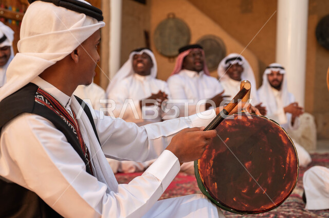 إظهار الولاء والحب للدولة السعودية، صورة مقربة من الجانب لرجل عربي خليجي سعودي يقوم بقرع الطبول احتفالا بتأسيس الدولة الأولى، الأحياء التراثية الطينية القديمة، إيماءات الفرح والاندماج مع الرقص وقرع الطبول احتفالا بيوم بدينا ١٧٢٧، ارتداء ازياء العرضه النجدية
