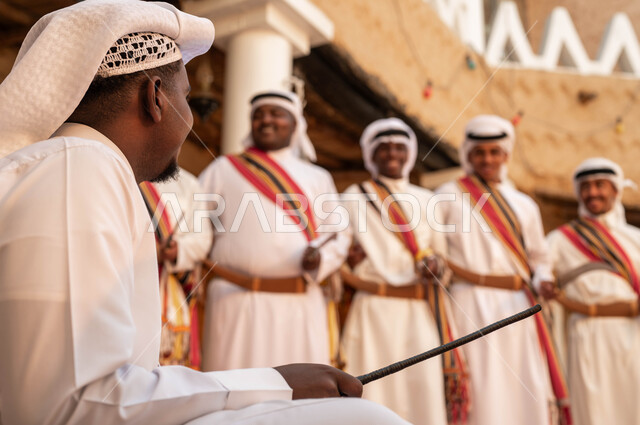 إظهار الولاء والحب للدولة السعودية، فرقة عرضة عربية خليجية سعودية يرتدون الزي الشعبي يقومون بالاحتفال بذكرى تأسيس الدولة السعودية ٢٢فبراير, الأحياء التراثية الطينية القديمة، إيماءات الفرح والاندماج مع الرقص الشعبي والأهازيج احتفالا بيوم بدينا ١٧٢٧