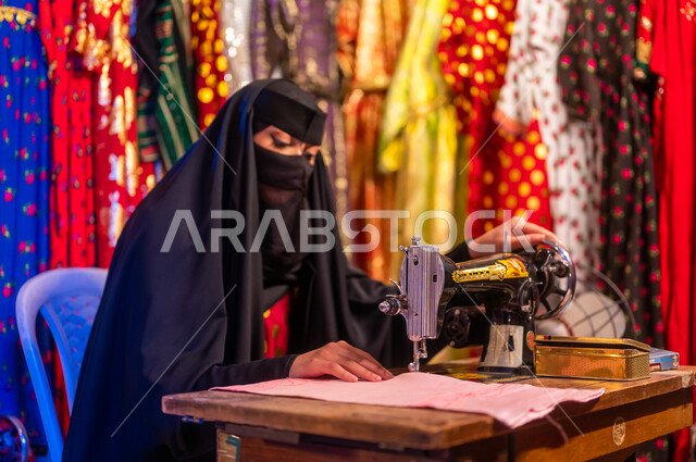 أعمال وحرف ومهن تقليدية نسائية, تأسيس الدوله السعوديه الاولى ٢٢ فبراير ،يوم التأسيس 1727 م، صورة مقربة لخياطة عربية سعودية خليجية ترتدي العباءة السوداء والبرقع تقوم بحياكة وخياطة القماش على الماكينة اليدوية في الأسواق الشعبيه القديمة في السعودية
